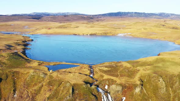 Aerial of a Little Blue Lake in Valley Surrounded with Golden Fields Iceland alt