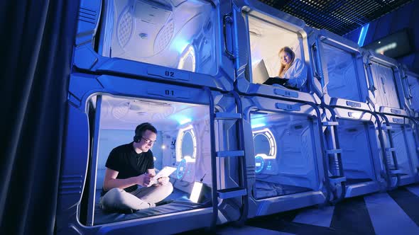 Rooms of a Capsule Hotel with Young People Inside of Them alt