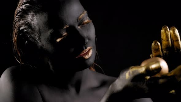 Portrait of a Young Woman with Black Paint on Her Face and Golden Hands and Lips alt
