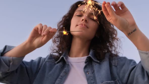 A young woman with sparklers is dancing and celebrating a holiday outside. Fireworks, bengal lights alt