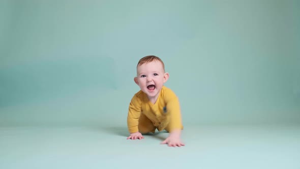 Happy toddler baby at the age of six months crawling on studio blue background. Funny child boy