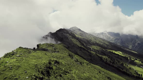 Aerial drone shot flying along grass covered mountains with a small trail leading along. More green alt