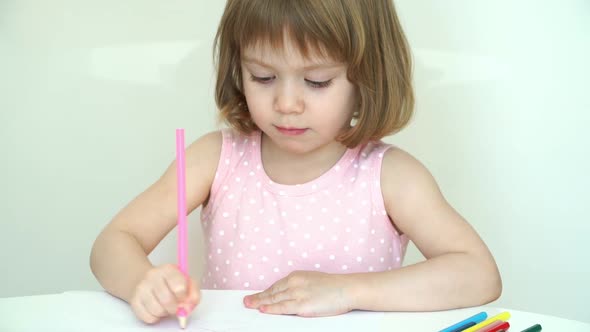 Little Smiling Child Girl Draws with Pencils on Paper Sitting at Table at Home