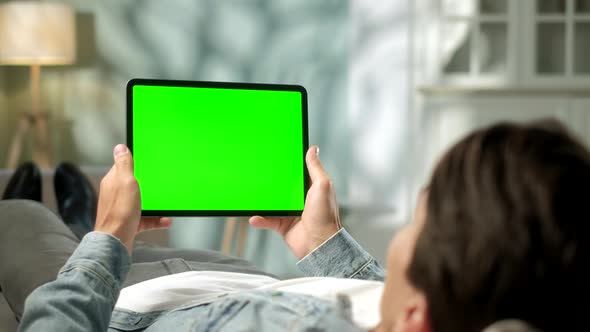 View From the Shoulder of Man Holding and Using Hand Gestures on Green Mock-up Screen Digital Tablet alt