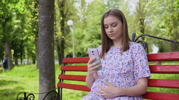 A Pregnant Woman is Sitting in a Summer Park and Reading Information for Pregnant Women on a alt
