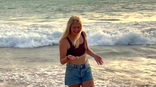 Young Happy Blonde Girl with Braces on Her Teeth Carries Crab Caught in the Ocean Against the