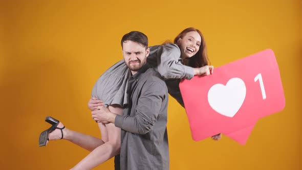 Cute Couple Man Woman Posing on an Isolated Background with a Heartshaped Sign They Ask to Put a Lot