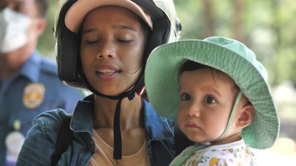 A Woman in a Motorcycle Helmet in Jean Clothes a Light Tshirt Stands and Shows a Child in a Summer