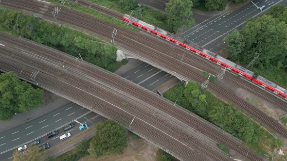 Birds eye view of a railway bridge crossing a big street with a red commuter train crossing the brid alt