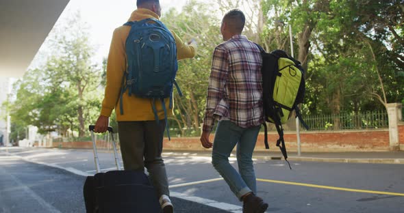 Back view of two happy mixed race male friends walking and talking down the street alt
