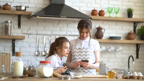 Mother and cute little daughter checking recipe in the internet and looking for the ingredients.