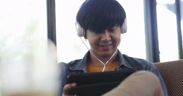 Happy young Asian man listening for music with headphone in living room. alt