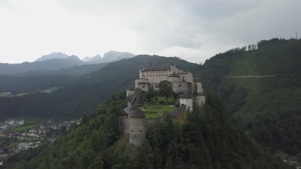 Aerial orbit of medieval Hohenwerfen Fortress on top of a steep hill, surrounded by pine forest and alt