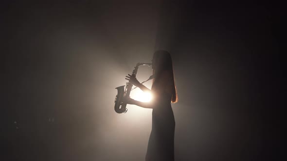 Young Beautiful Girl in a Dark Dress Plays on a Golden Shiny Saxophone on Stage alt