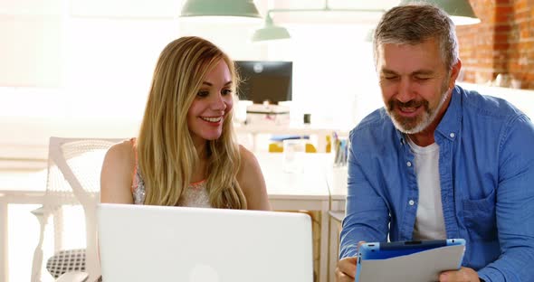 Male and female executives discussing over digital tablet at desk alt