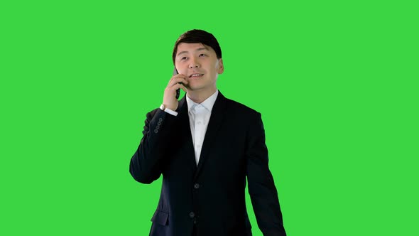 Asian Businessman Walks Talking on Mobile Phone on a Green Screen Chroma Key