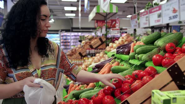 Young Woman Housewife in a Grocery Store Buys Takes Ripe Tomatoes From the Shelf and Puts Them in a alt