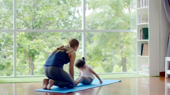 Young mother training little daughter for sit-up exercise