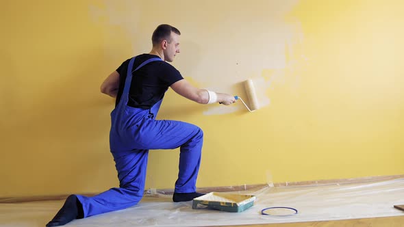 Young man painting wall with roller brush while renovating his apartment. alt