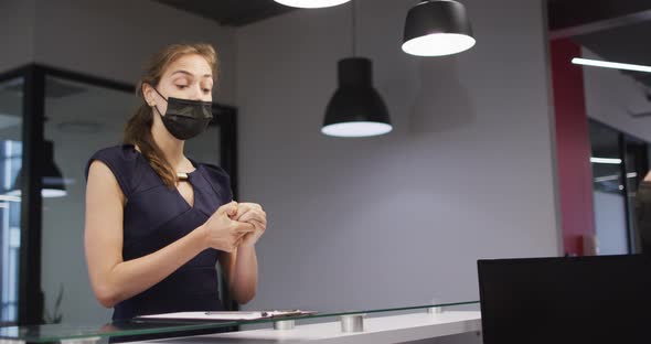 Caucasian woman in face mask disinfects hands and signs in at office reception desk alt