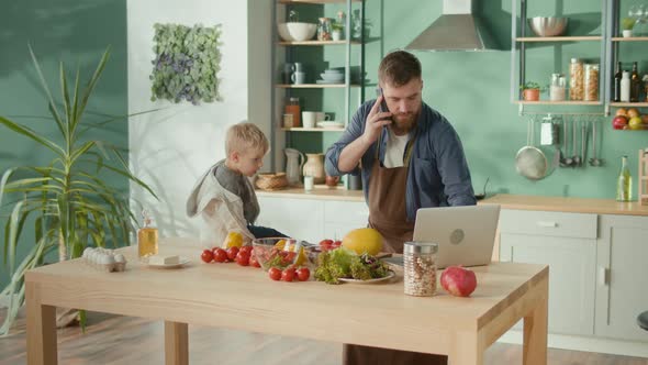 Father With Son Cooking Breakfast Cutting Vegetables for Salad in Kitchen alt