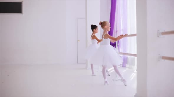 Two Children Ballerinas in White Tutus is Warming Up Near Barre in Ballet Class