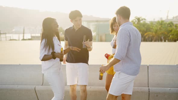 Group of Young Positive Diverse Friends Enjoying Summer Sunset Outdoors Dancing and Drinking Beer alt