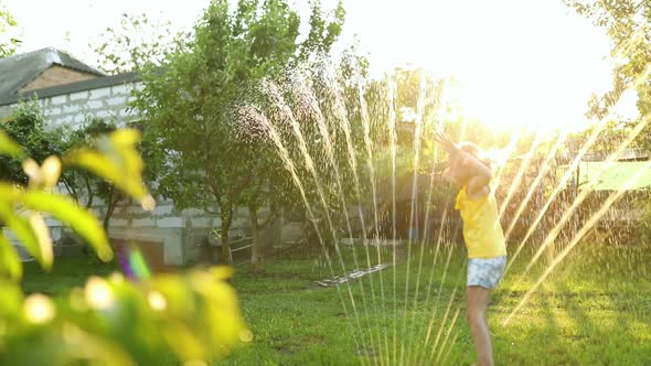 Happy kid girl playing with garden sprinkler run and jump, summer