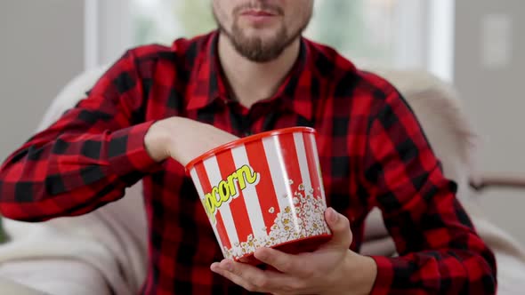 Smiling Carefree Young Man Eating Chips From Popcorn Box at Home alt