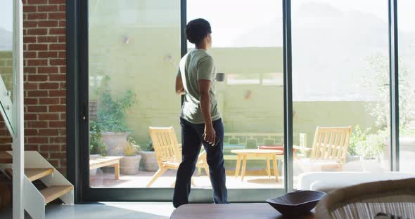 African american man using smartphone and drinking coffee at home alt
