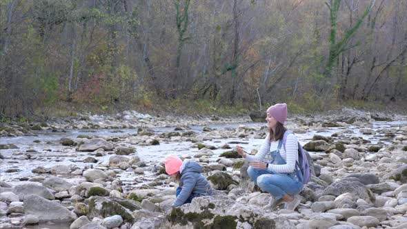 Young Mother with Little Daughter Is Throwing the Stones Into the Mountain River