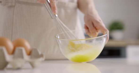 Process of Mixing Eggs with a Whisk in a Glass Bowl on Kitchen at Home alt