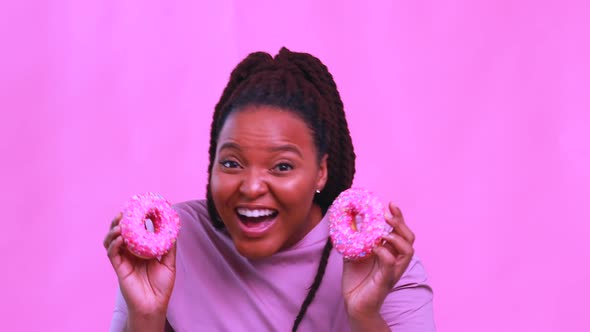Multicultural Female Holding Delicious Sweet Donut in Pink Studio Background alt