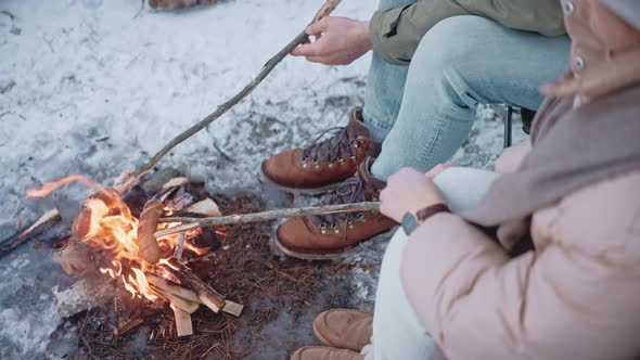 People are Roasting Sausages on Sticks on a Campfire in the Woods in Winter