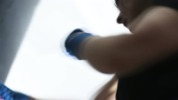 a Young Female Boxer in Bandages on Her Hands Hits a Punching Bag alt