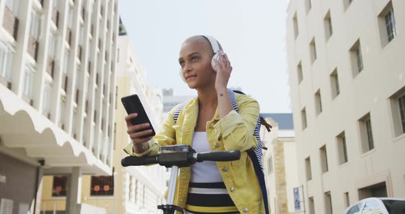 Mixed race woman listening music on the street on her e scooter alt