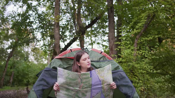 A Female Tourist Studies the March on a Map While Sitting in a Tent in the Woods