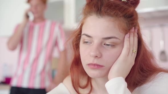 Close-up Portrait of Gorgeous Sad Woman Holding Head with Hand. Blurred Man Talking on the Phone at alt