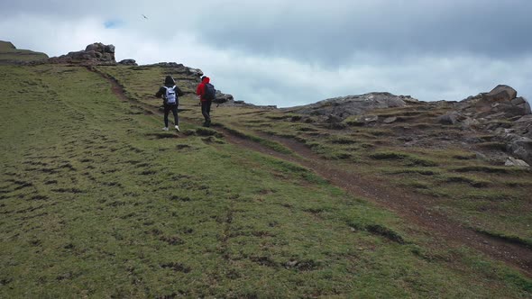Two Hikers Trekking Near a Cliff Surrounded By Scenery of Faroe Islands alt