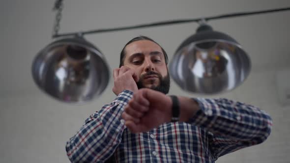 Bottom Angle View of Confident Handsome Middle Eastern Man Checking Time on Watch Talking on the alt