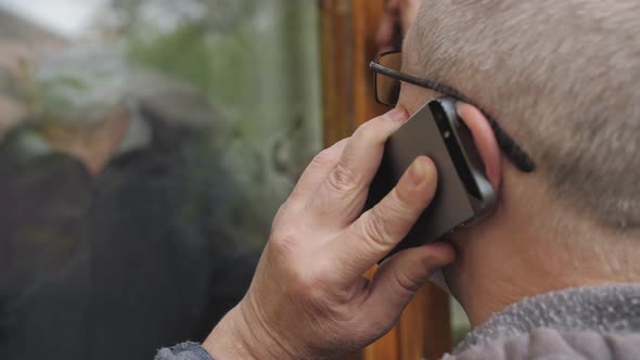An Elderly Woman Is Talking on a Cell Phone with an Elderly Man in an Antiviral Mask Who Is Standing alt