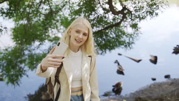 Smiling Young Woman Tourist Makes a Selfie on the Background of a Pond with Ducks