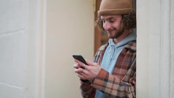 Positive curly-haired man texting by phone alt