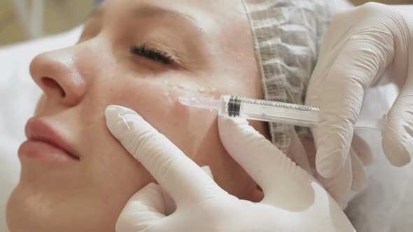 Doctor beautician makes injections in the face of the female patient