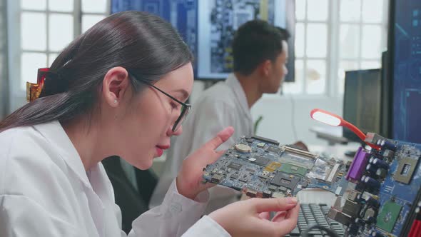Development Facility: Beautiful Asian Female Engineer Inspects Printed Circuit Board Motherboard alt