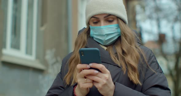Portrait of Woman in Medical Protective Mask Typing By Mobile Phone Outdoors. Close Up Cheerful Girl alt