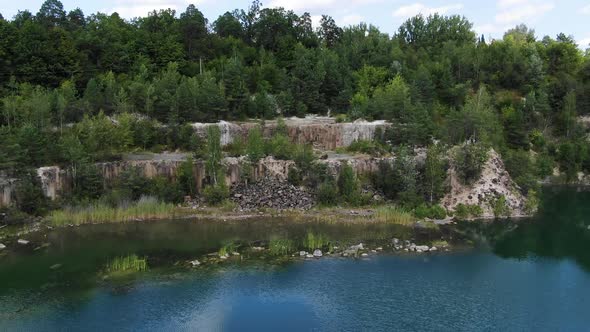 Aerial View of lake with Beautiful Water in a Quarry Surrounded by Forest Tracking Backward alt