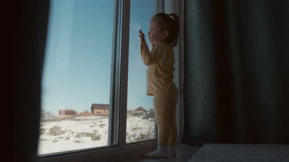 The Kid Stands Near the Window of the House and is Sad alt
