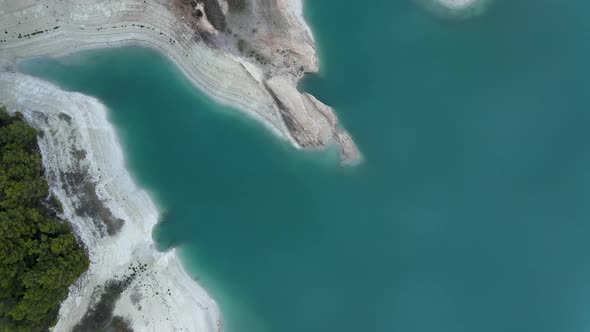 Forward Aerial of Still Lake Trees and Eroded Stony Coastline Spain alt