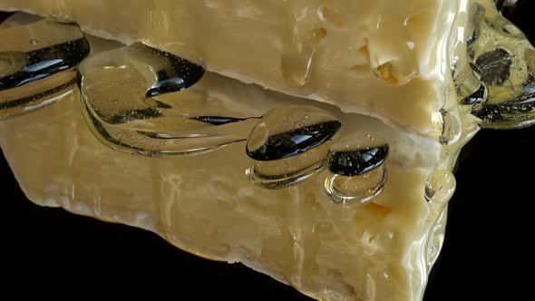 Drops of honey dripping from Brie cheese on a mirrored black background. alt